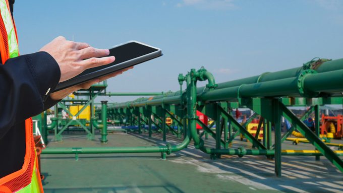Person in a high-visibility vest using a tablet near green industrial pipes and infrastructure.