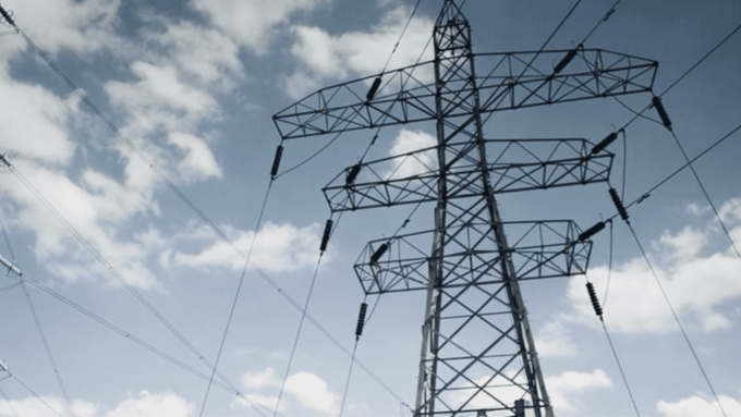 Two tall electricity pylons with multiple power lines set against a partly cloudy blue sky.