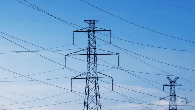 A series of electrical transmission towers stand in a clear blue sky, with multiple power lines stretching between them.