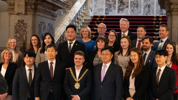 A group of formally dressed individuals posing for a photo in front of a staircase in an ornate building, reminiscent of the grand architecture found in Belfast.