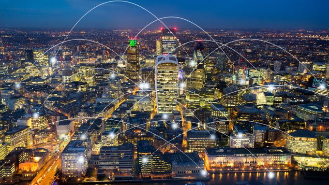 Aerial view of a cityscape at night with multiple white arcs and dots superimposed, representing Urban Artificial Intelligence connected networks.