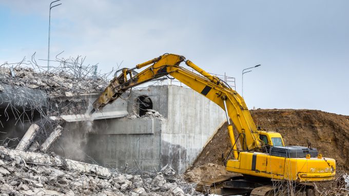 Professional demolition of reinforced concrete structures using industrial hydraulic hammer. Rods of metal fittings. Wreckage and crumbles of concrete.