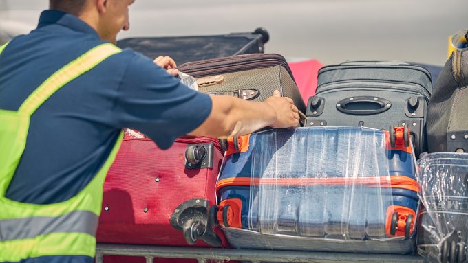 A member of airport staff unloads baggage from a trolley to be put in the hold